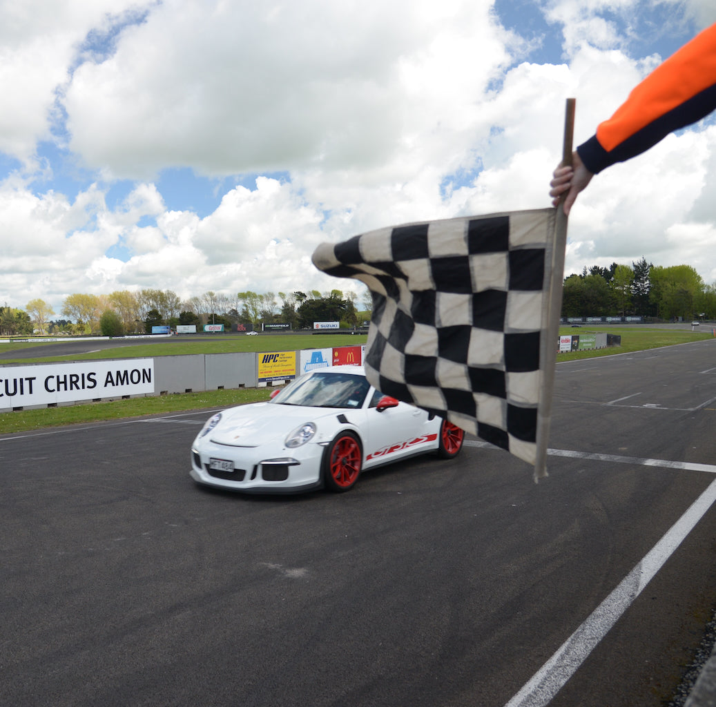 Race car crossing the finish line with a checkered flag at Circuit Chris Amon.